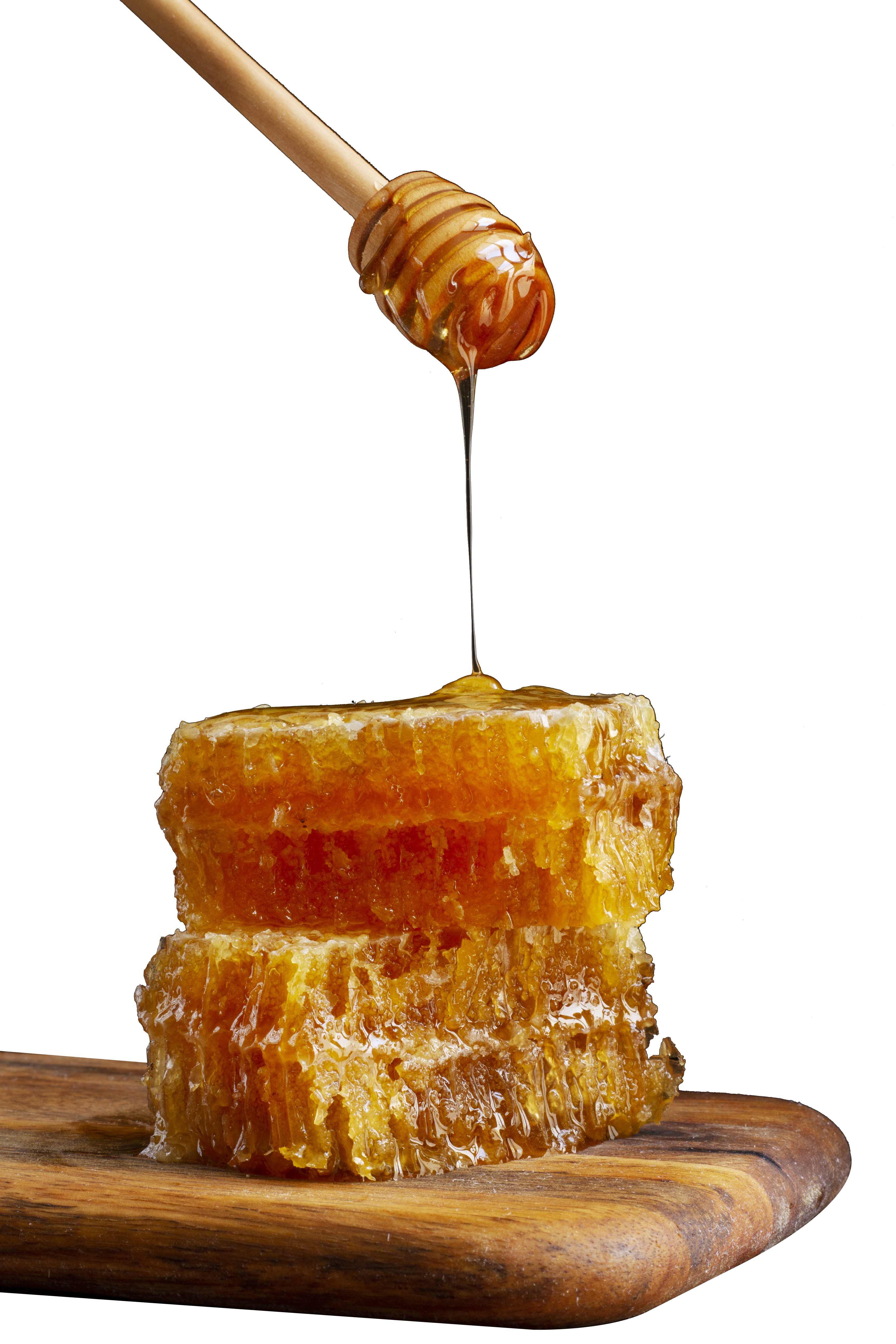 Honey dripping from dipper onto stacked honeycomb on wooden board